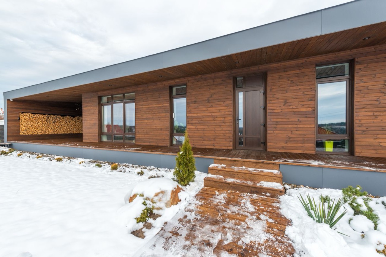 Maison en bois avec stock de bûches sous la neige, chauffage au bois en hiver